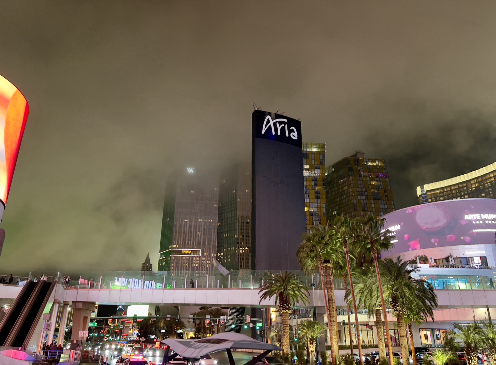 The ARIA sign atop its tower in low cloud at night, seen from the Strip pedestrian bridge