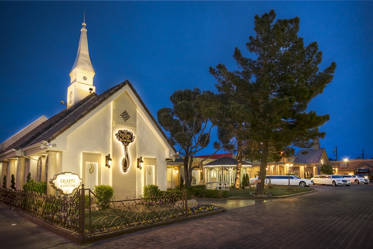 Chapel of the Flowers on Las Vegas Boulevard at twilight, white steeple lit, with limousines parked beside the chapel